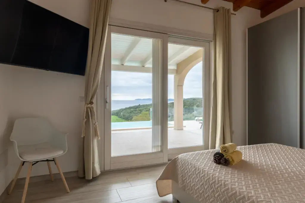 Bright bedroom with sliding glass doors opening to a terrace with sea and pool view