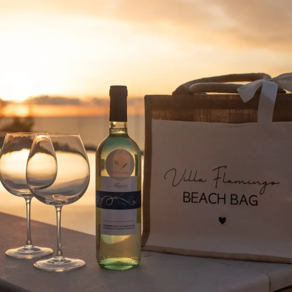Wine bottle, two glasses, and a beach bag with sunset view by the pool