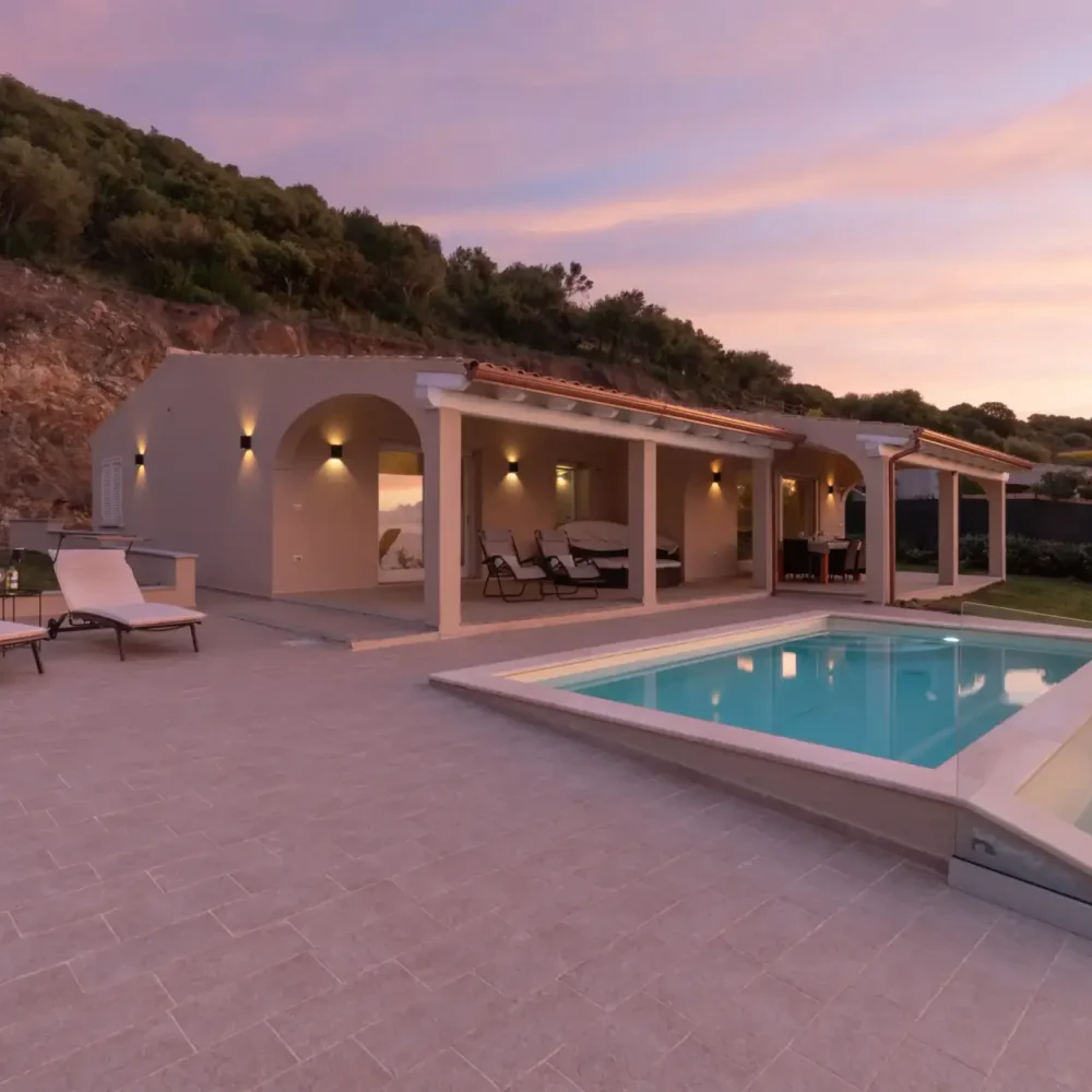 Modern holiday villa with illuminated terrace and pool at sunset