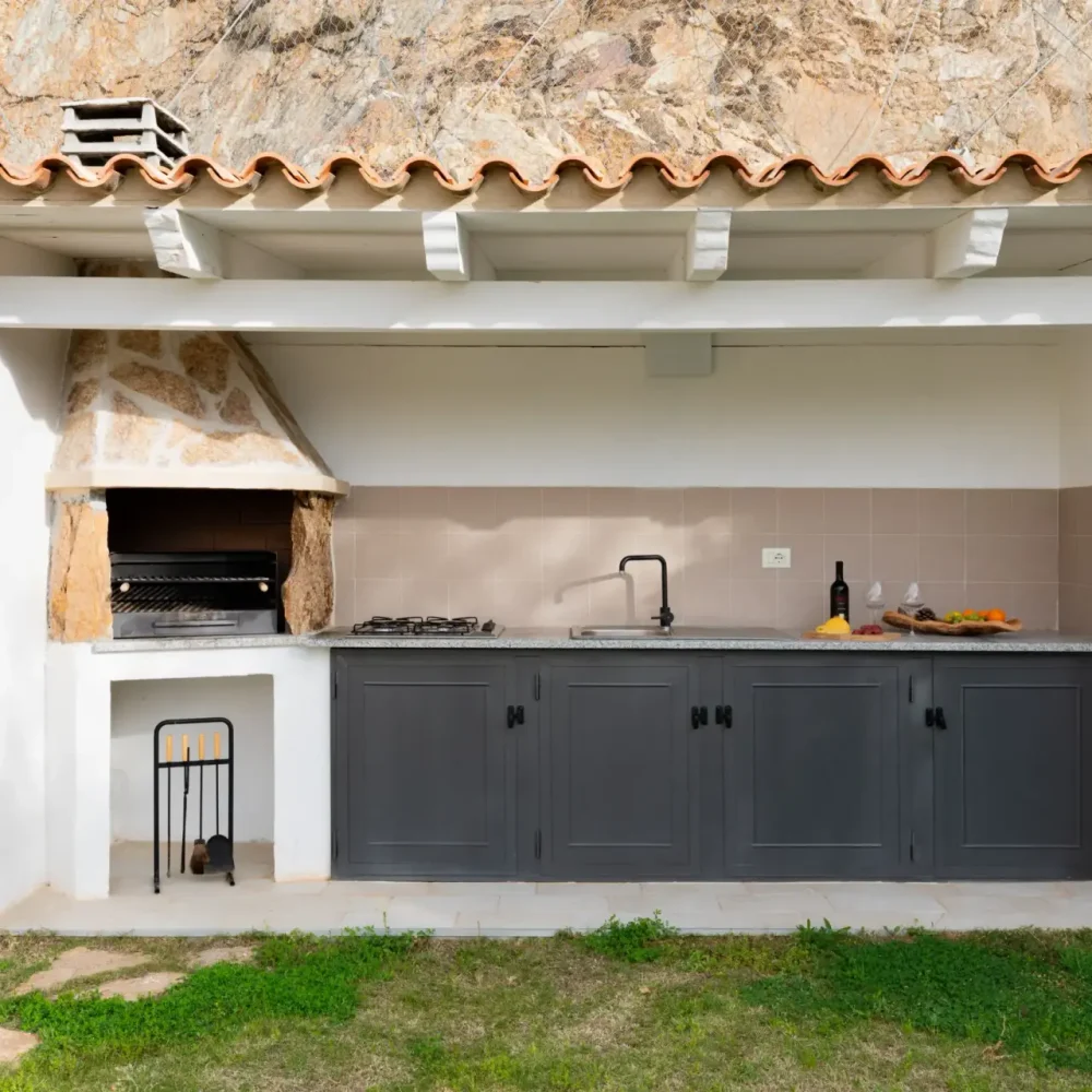 Outdoor kitchen with built-in grill, sink, and countertop in front of a stone wall