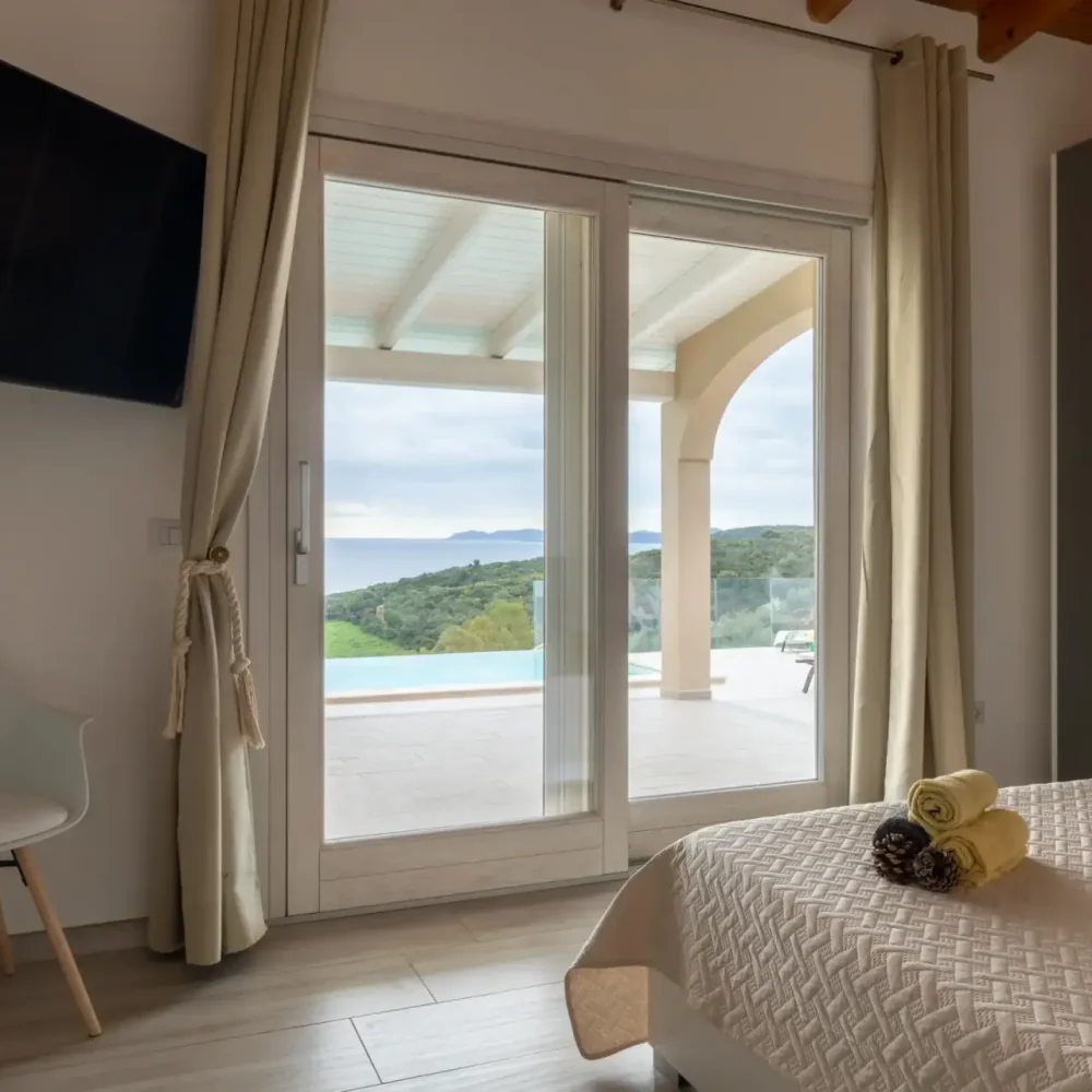 Bright bedroom with sliding glass doors opening to a terrace with sea and pool view